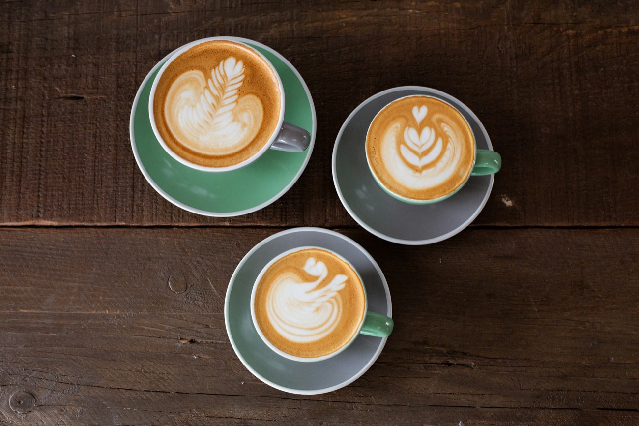 Tres cafés con leche con dibujo de espuma, vistos desde arriba
